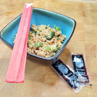 bowl of vegetable fried rice with chopsticks and soy sauce packets