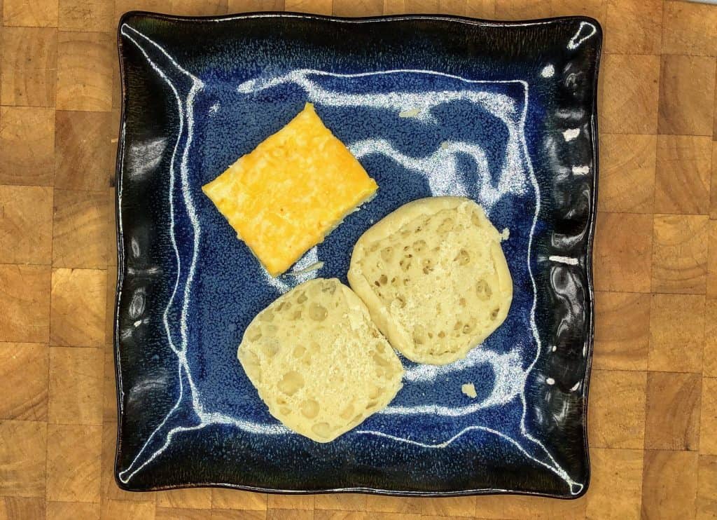 english muffin open on plate next to egg square with cheese