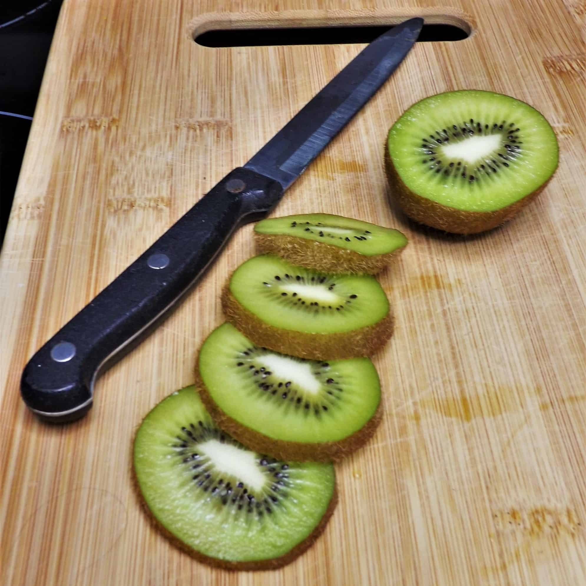 sliced kiwi next to a knife on a cutting board