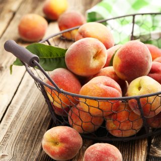 Ripe peaches fruit in basket on a brown wooden background