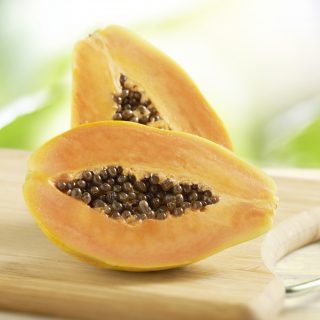 Halved fresh tropical papaya with pips displayed on a wooden cutting board