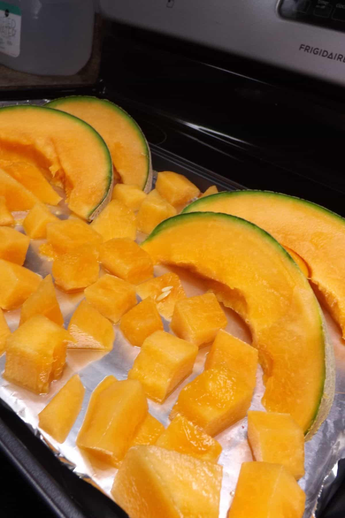 Slices and chunks of cantaloupe on a cookie sheet.